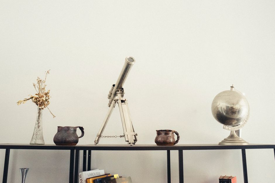 A modern shelf displaying a telescope, globe, books, and vases for a classy decor.